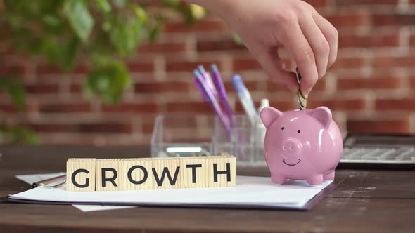 Table Wooden Cubes That Make Up the Word Growth Hand Puts Coins in a Piggy Bank alt