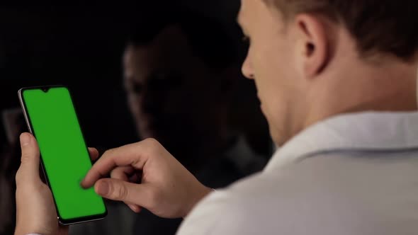 Young man with a phone moves his finger across the screen, chroma key, back view alt