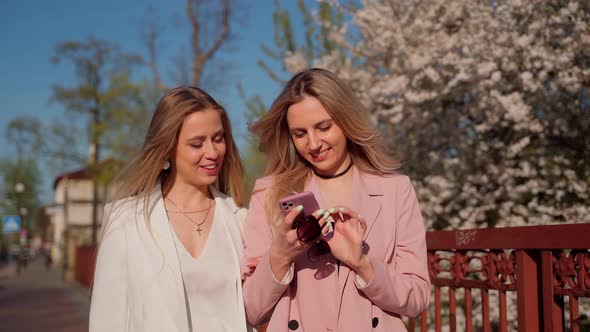 Two females persons looking at smartphone walking smile and laugh. Young adult women spending time alt