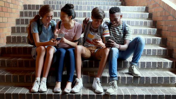 Classmates sitting on staircase and using mobile phone alt