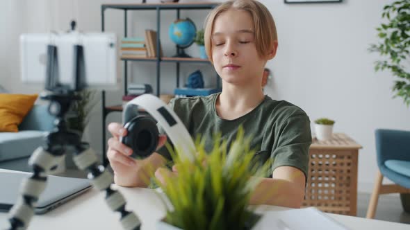 Teenage Boy Vlogger Recording Video About Headphones Talking and Holding Device Using Smartphone alt