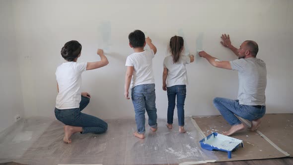 Caucasian Family Paints the Wall with Paint Brushes Dad Mom Son and Daughter Together Make Repairs