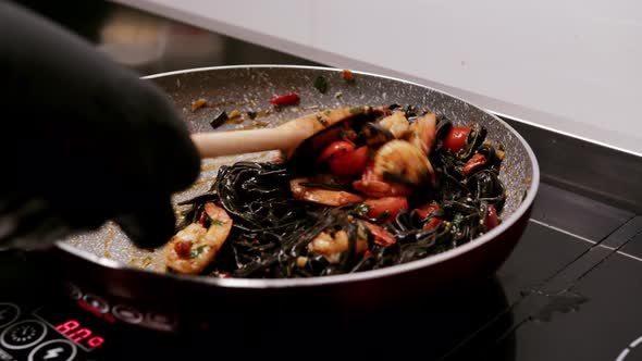 Close up view of pasta been prepared with black macaroni, shrimps, coctail tomatoes and herbs over i alt