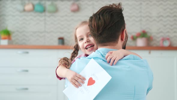 Cute little girl giving a card to dad for a holiday in the living room alt