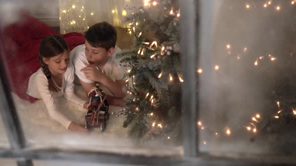 Festive Christmas Holidays scene - children play with sleigh filmed through window with snow outside