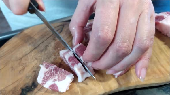 A woman cuts a large piece of pork meat with a knife. Meat with fat layers, pork neck. 4k alt