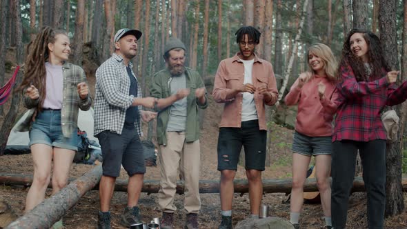 Playful Young People Dancing Around Campfire in Woods During Recreational Trip Outdoors alt