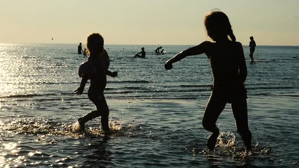 Kids Silhouettes Running On The Sea Water, Children Play On Sea Shore. Sun Flare