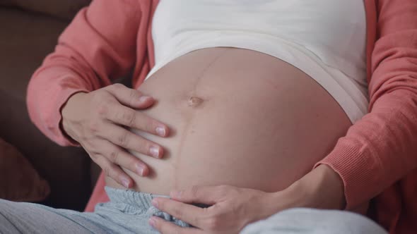 Young Asian Pregnant woman holding her belly talking with her child feeling happy smiling.