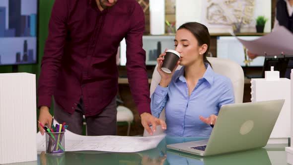 Female Chief Architect Taking a Sip of Coffee and Helping Her Colleague alt