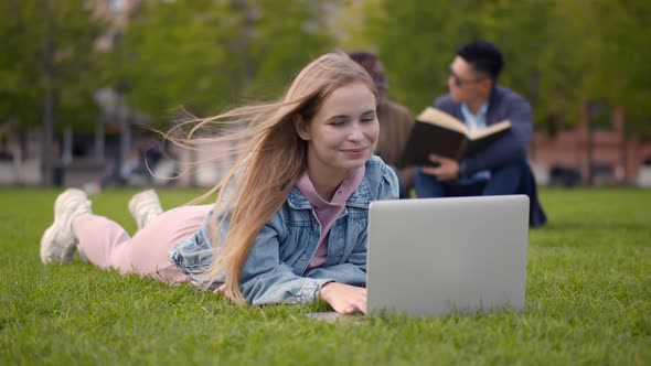 Student Woman Smiling Using Computer Laptop Lying on Grass at University Campus alt