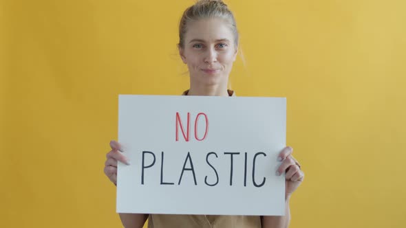Portrait of Female Activist Holding No Plastic Sign and Smiling on Yellow Background alt