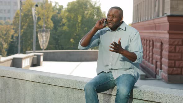 Adult Mature African American Man Sitting Outdoors Holding Cell Phone Irritably Angry Talking to alt