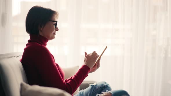 Relaxed Young Woman in Glasses Using Her Smartphone While Sitting on the Sofa alt