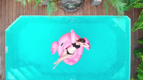A Woman Swims on a Pink Flamingo in the Pool  Aerial View alt