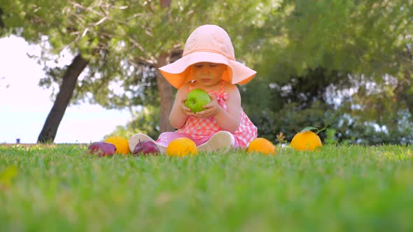 Little Princess Playing with Fruits Outdoor. Happy Childhood Concept. Toddler Sitting on Green Grass