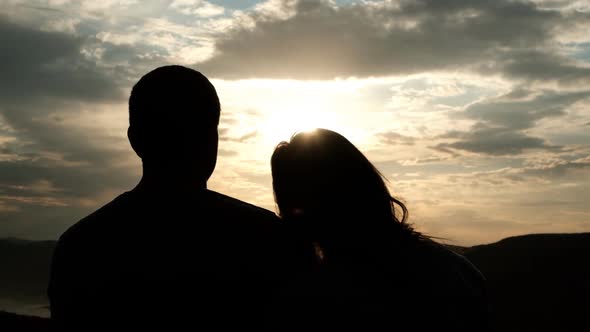 Silhouettes of a Couple of Young People at Sunset. A Woman Puts Her Head Gently on Her Man's