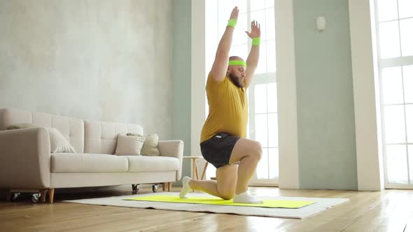 Plump Man Doing Squats in Lunges Exercise with Hands Up Standing on Mat at Home