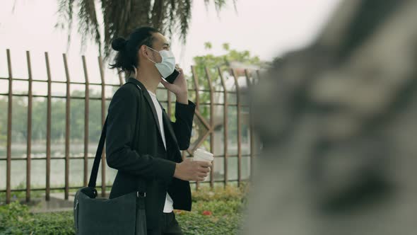 Asian businessman wearing a surgical mask holding coffee cup and talk phone.