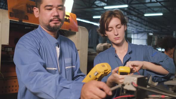 Two professional engineers inspect machines' electric systems at the factory. alt