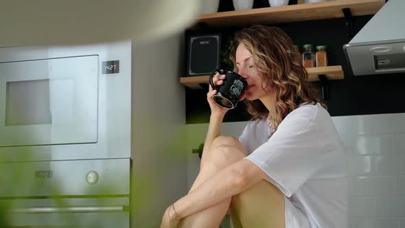 Young pretty woman drinks coffee sitting at her kitchen at home