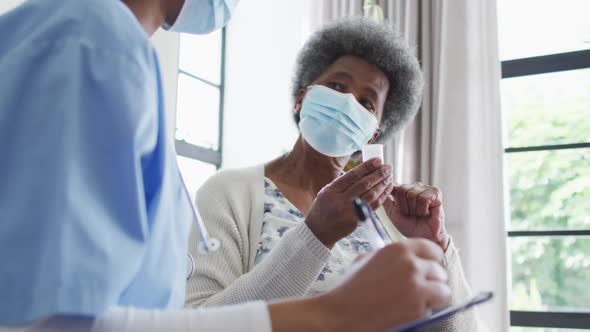 African american female doctor and senior female patient in face masks alt