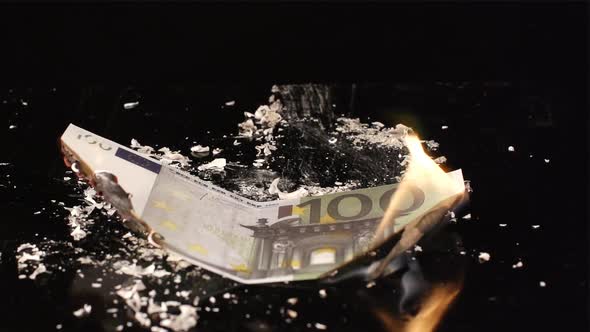 One hundred euro is flaming and falling on a black table