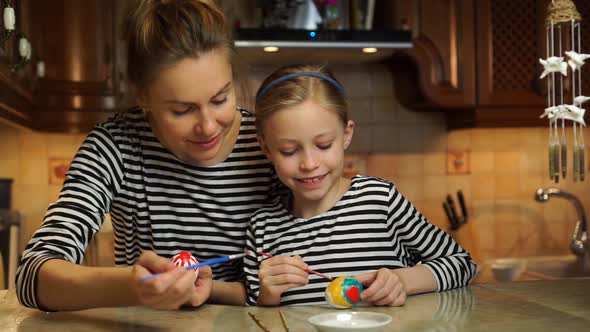Beautiful Caucasian Mother and Child Daughter in Striped Dresses Paint Easter Eggs Having Family Fun alt