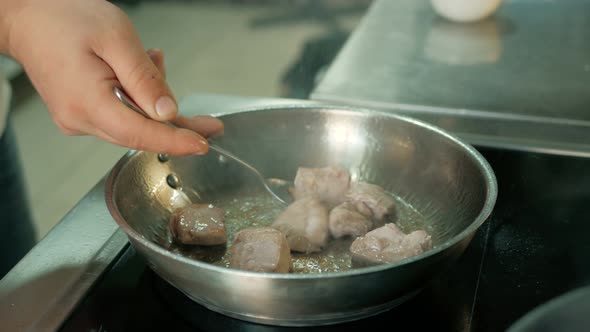 chef is frying meat in a frying pan in a restaurant kitchen. alt
