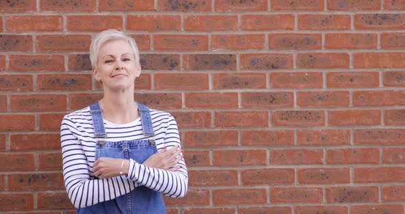 Mature woman in dungarees standing in front of brick wall