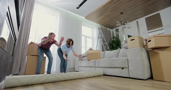 Young Caucasian Couple Spreads a Carpet in Living Room in a New Apartment alt