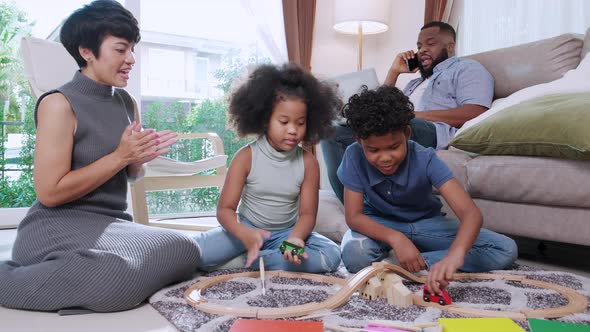 Happy African American parent and kid son, girl playing toy cars racing at home