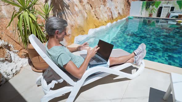 Slow Motion Side View Man Lying By Pool with Laptop Computer Man Giving Online Interview Speaking on alt