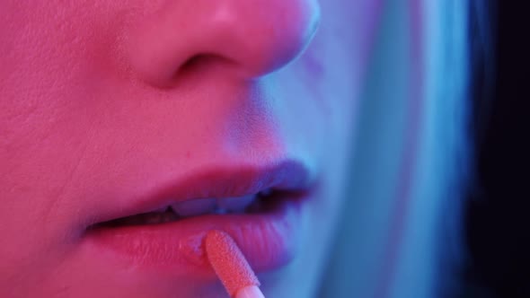 Young Woman Paints Her Lips with Bright Lipstick in Neon Light