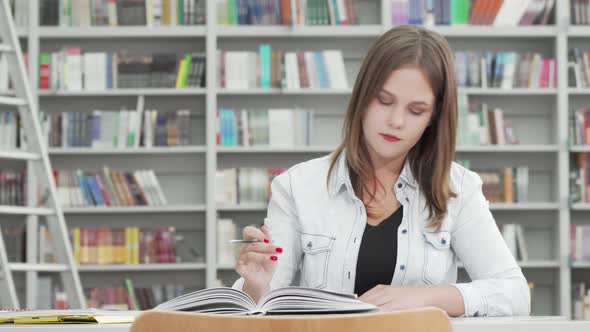 Female Student Writing in Her Textbook at Campus Library