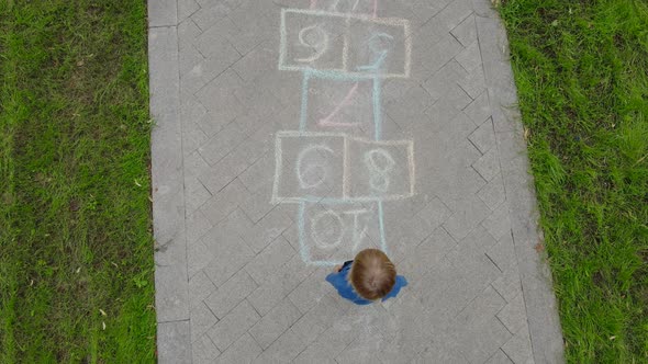 Aerial view of little boy jumping by hopscotch drawn on asphalt
