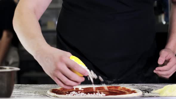 Chef sprinkles pizza with mozzarella cheese in the kitchen of a pizzeria. Pizza to order. alt