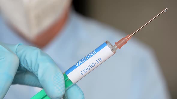 Close up of a researcher with face mask holding a syringe with coronavirus vaccine