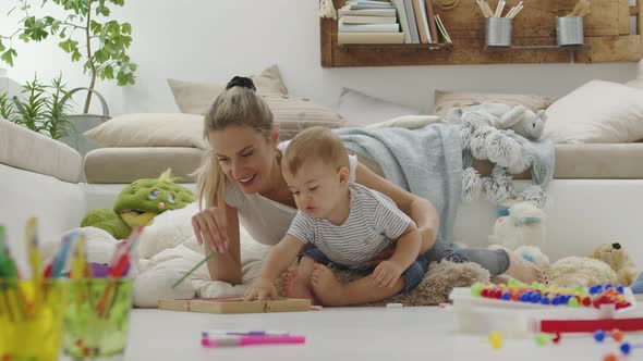 Happy smiling mom plays with her baby, with colorful pencils and chalks