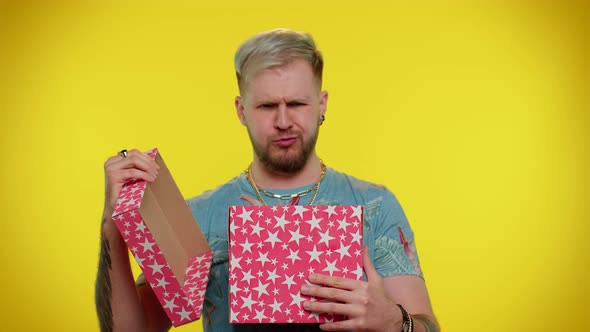 Young Man Unwrapping Birthday Gift and Expressing Disappointment Dislike Bad Present Dissatisfied alt