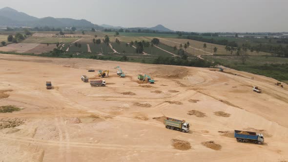 Aerial of Trucks loaded with sand on Construction site, Excavators digging the soil, Aerial Orbiting alt