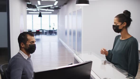 Mixed race woman in face mask has temperature checked by male colleague at office reception desk alt