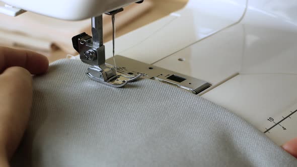 Woman hands with gray fabric sewing with a sewing machine. Women's hands sew on a sewing machine.