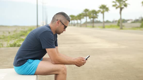 Attractive Man 3040 Years Old Sitting on the Waterfront Looking at the Phone Screen