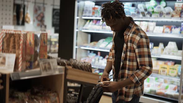 Male Customer Chooses Smth in the Grocery Store Put It to the Cart alt