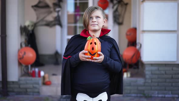 Happy Confident Caucasian Boy in Halloween Vampire Costume Standing with Jack O'Lantern Outdoors alt