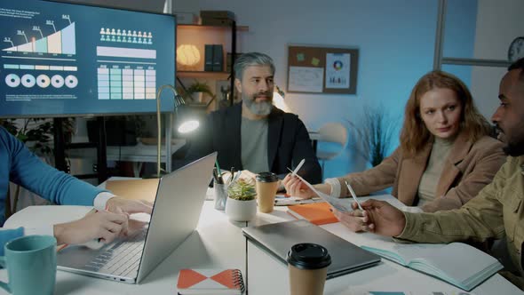 Zoomin of Businessman Speaking to Colleagues Diverse Team During Meeting in Office at Night alt