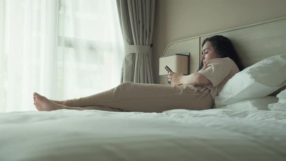 Thoughtful Young Caucasian Woman Using Smartphone While Sitting on Bedroom alt