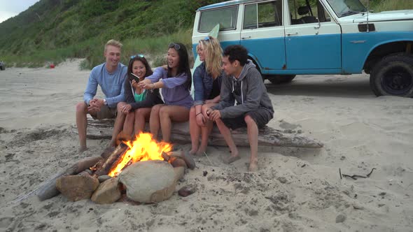 Group of friends at beach hanging out by campfire alt