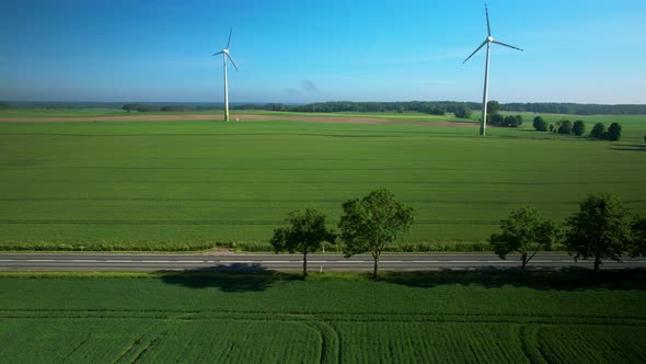 White truck driving along rural countryside road with wind turbines blades rotating on agricultural alt